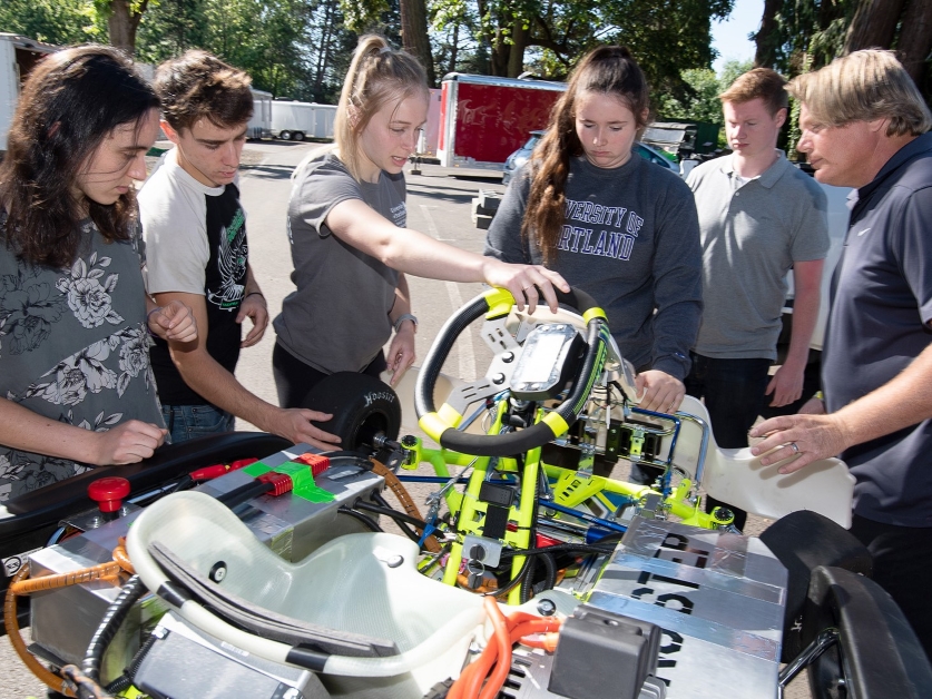 A group of UP students work on a prototype electric vehicle on a sunny day outdoors