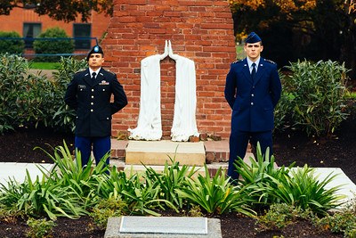 two students in ROTC uniforms stand beside the Praying Hands memorial wall