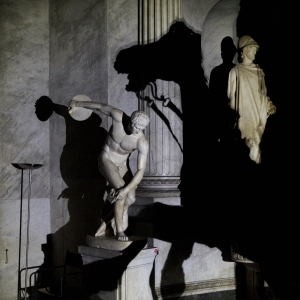 Sculptures cast shadows on the walls of a museum at night.