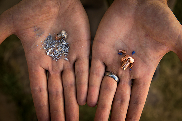 Hands holding shattered lead bullet fragments and copper bullet fragments.