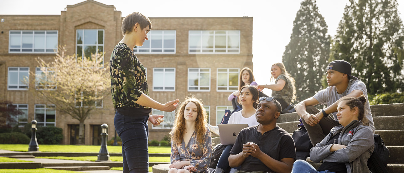 A tour guide talks with students sitting on outdoor steps on UP's campus