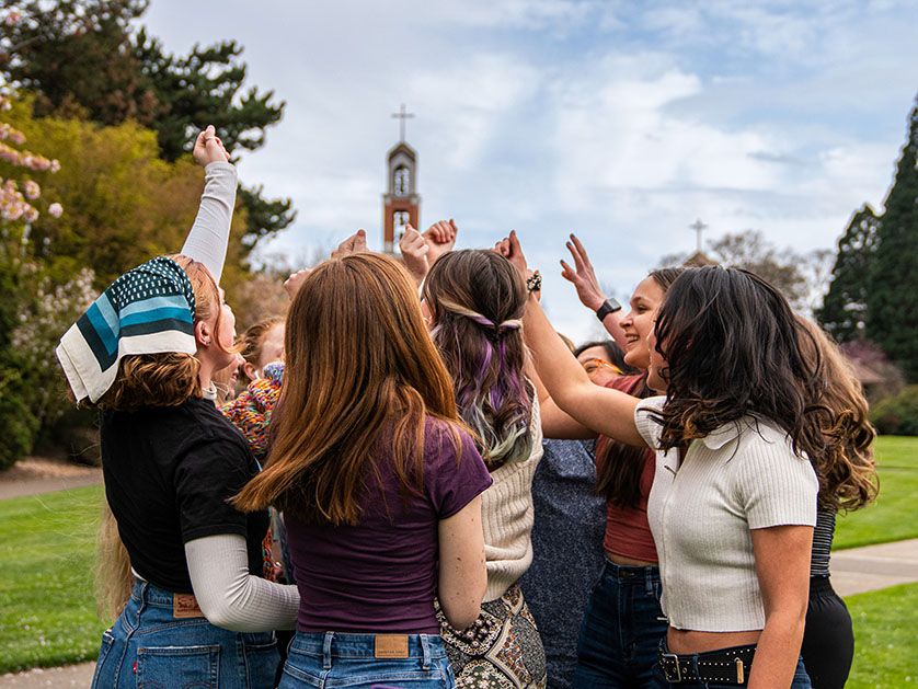 A group of young people high-five with the bell tower in the background.