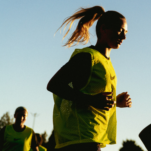 A close-up view of a UP soccer player wearing a yellow jersey, running on the field in the glow of the setting sun.