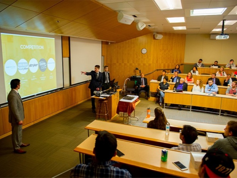 Student presenting business plan in front of judges in a tiered classroom in Shiley Hall