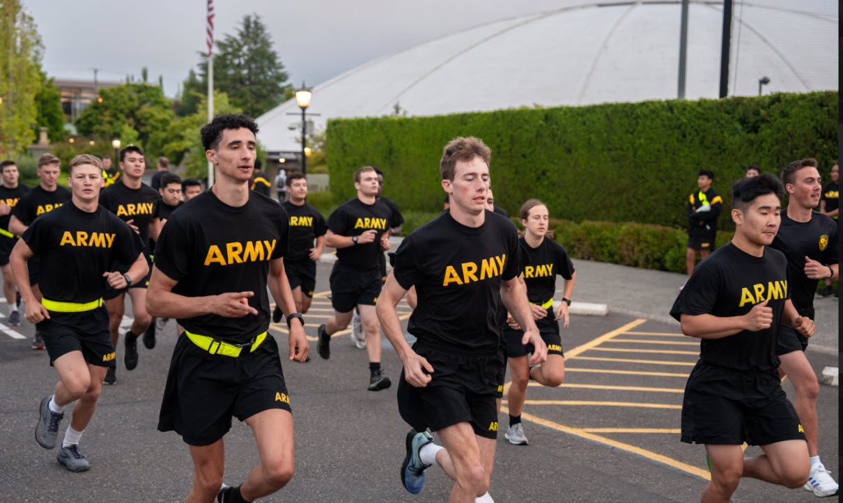 Rotc cadets running on campus past the entrance gate wearing army shirts 