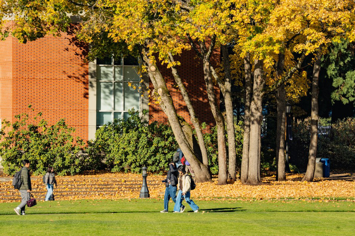 Students walking on the quad on a sunny fall day as the leave on the trees change color.