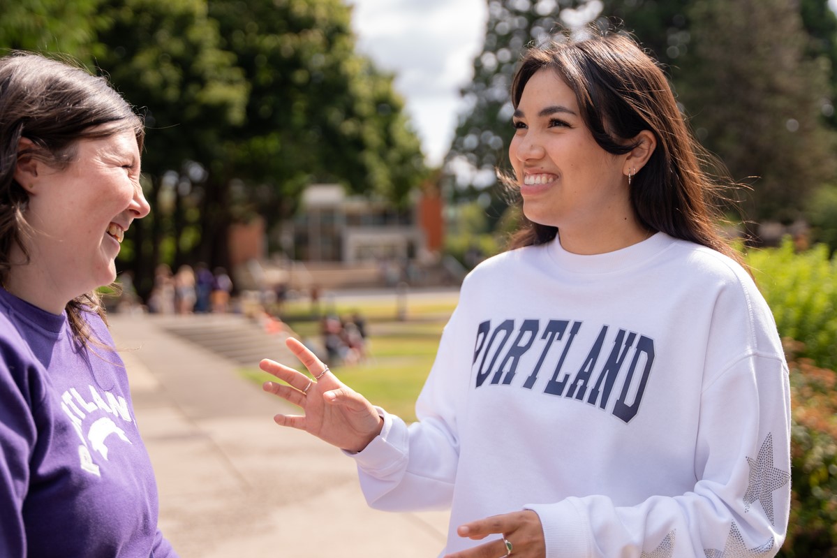 Two students cheerfully converse during a summer day on the quad