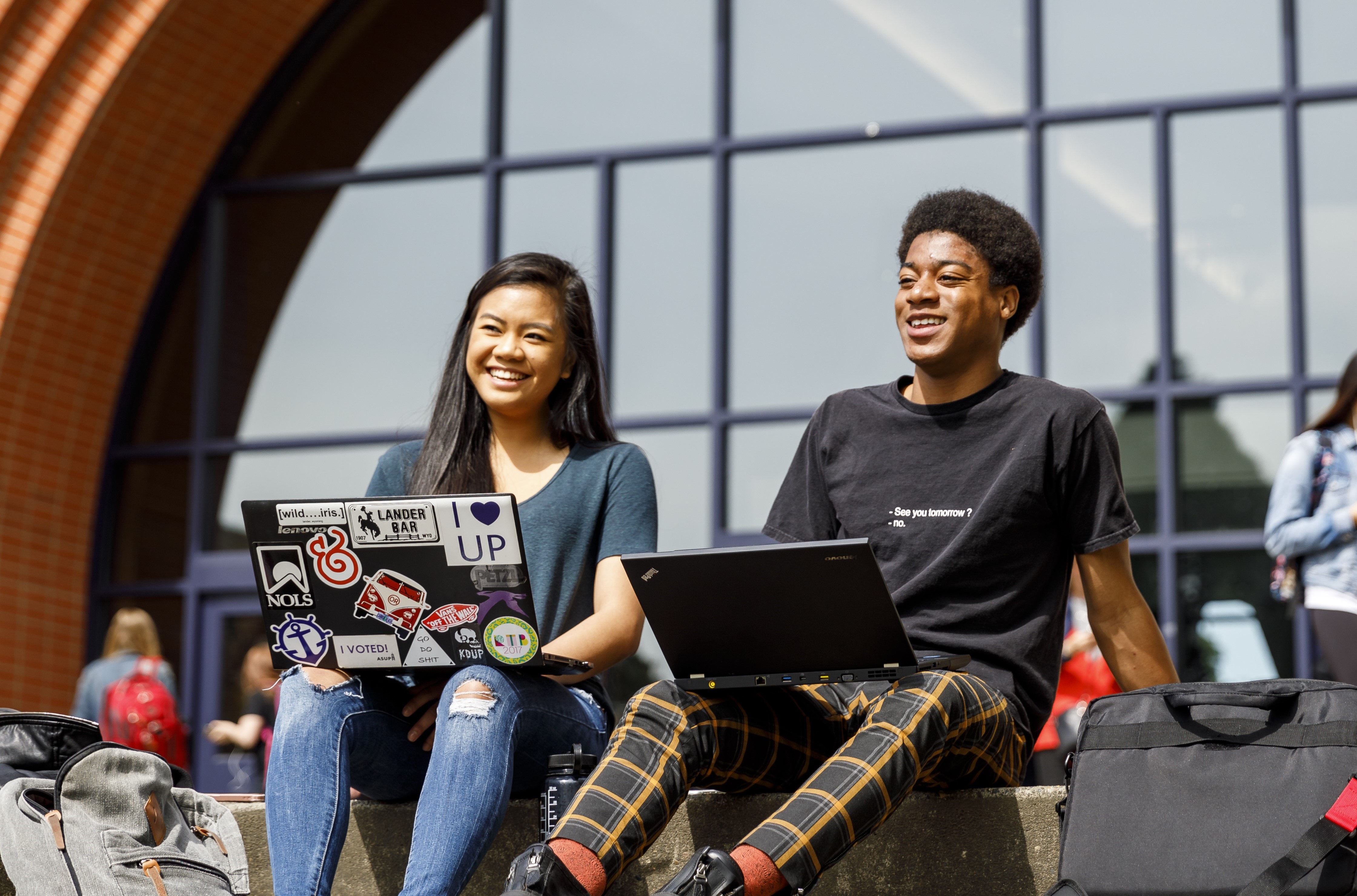 Two students with laptops sit on the steps of Franz Hall