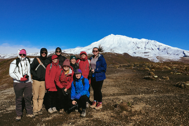 A group of UP students pose and smile in front of a snowy white mountain in New Zealand during a study abroad trip.