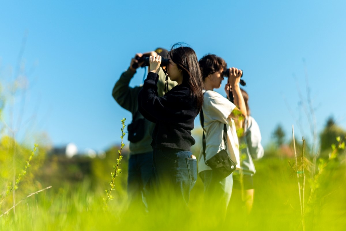 Biology students stand in a circle peering through binoculars at wildlife on the river campus at UP.
