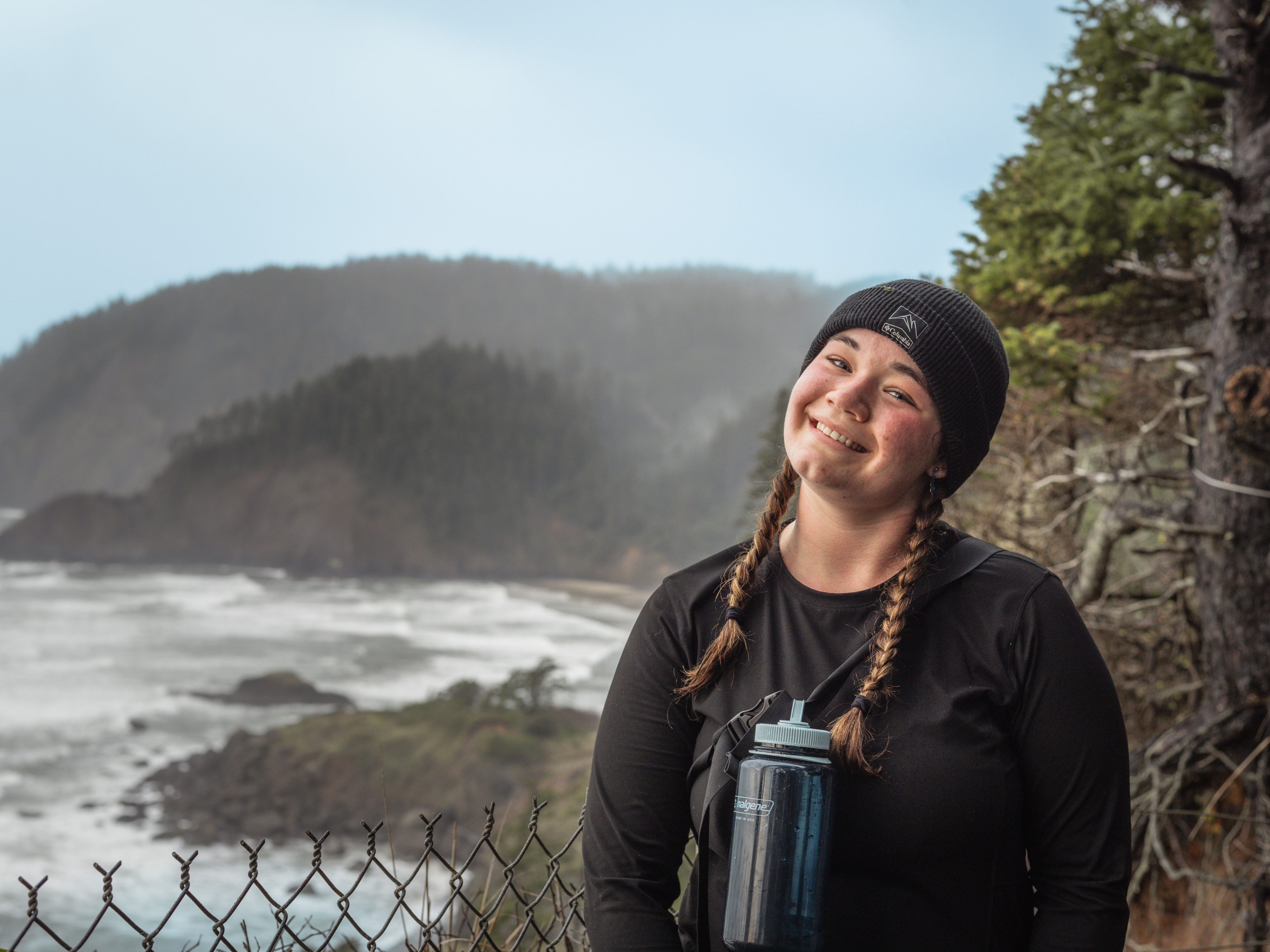 A UP student poses on a hiking trail with the pacific ocean in the background