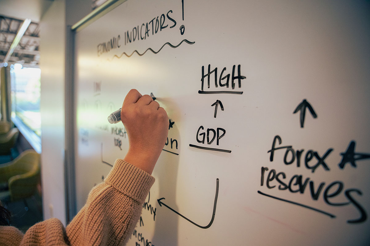 A student's hand writes an economic equation on a white board in the Clark Library.