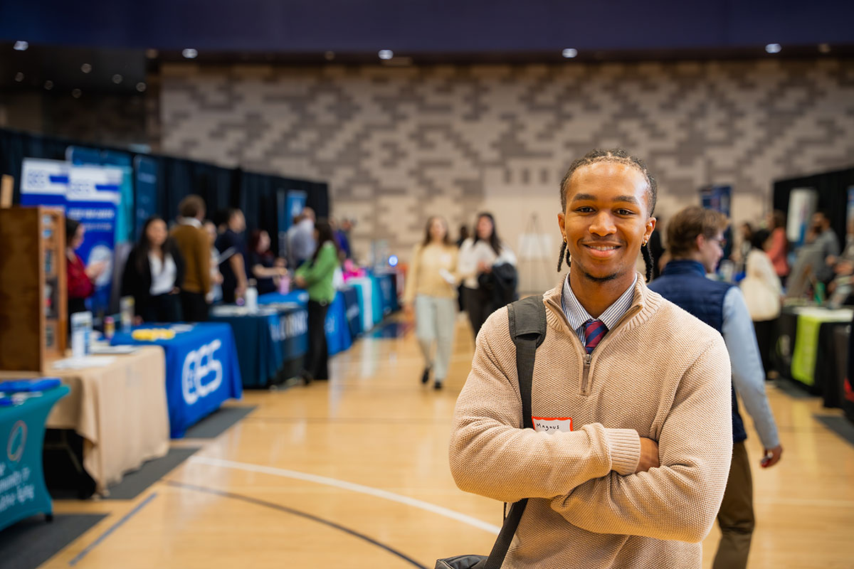 A smiling UP student stands with arms crossed in the middle of the internship career fair at Beauchamp center