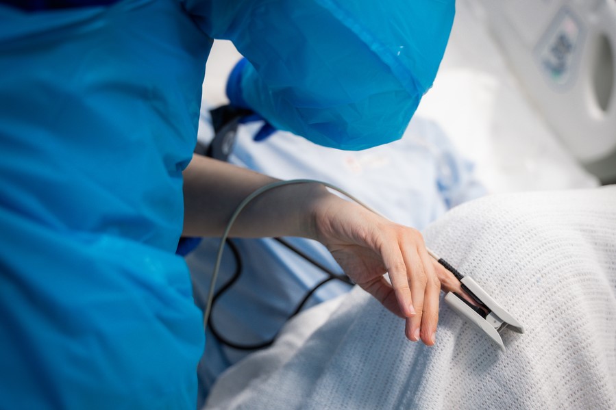 Close up of healthcare worker tending to a patient whose hand is visible and fitted with an oxygen sensor