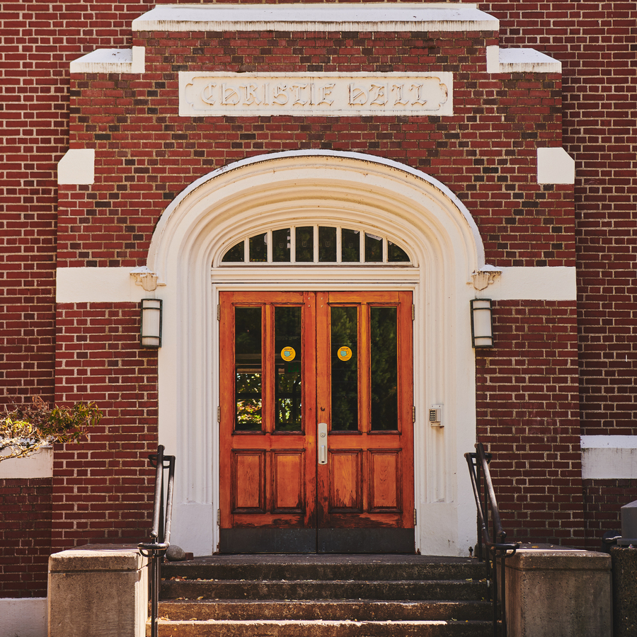 Close-up view of the entrance to Christie Hall, an historic red brick university building featuring a white arched window and an aged engraved sign above it.