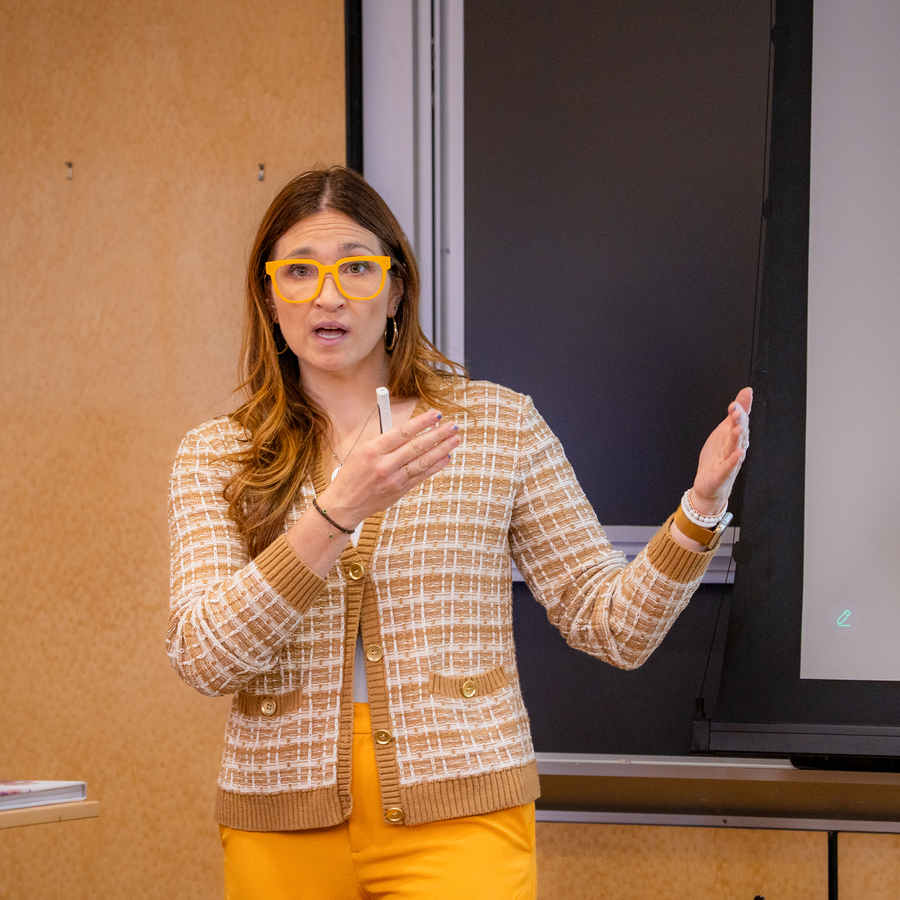 A UP accounting professor in a brown and white checkered cardigan stands in front of a projector screen during a lecture.