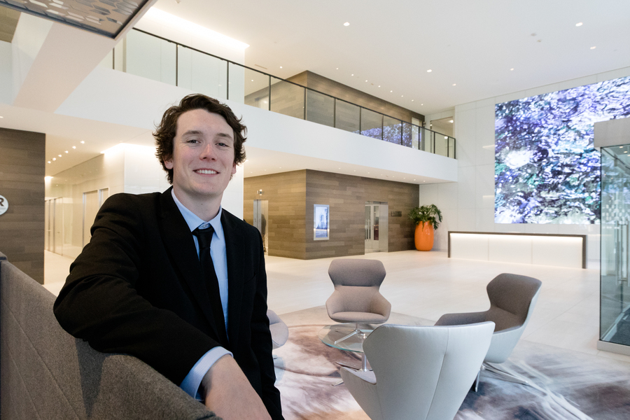 A low angle image of a smiling UP student dressed in business attire and seated in a modern office lobby during an internship.