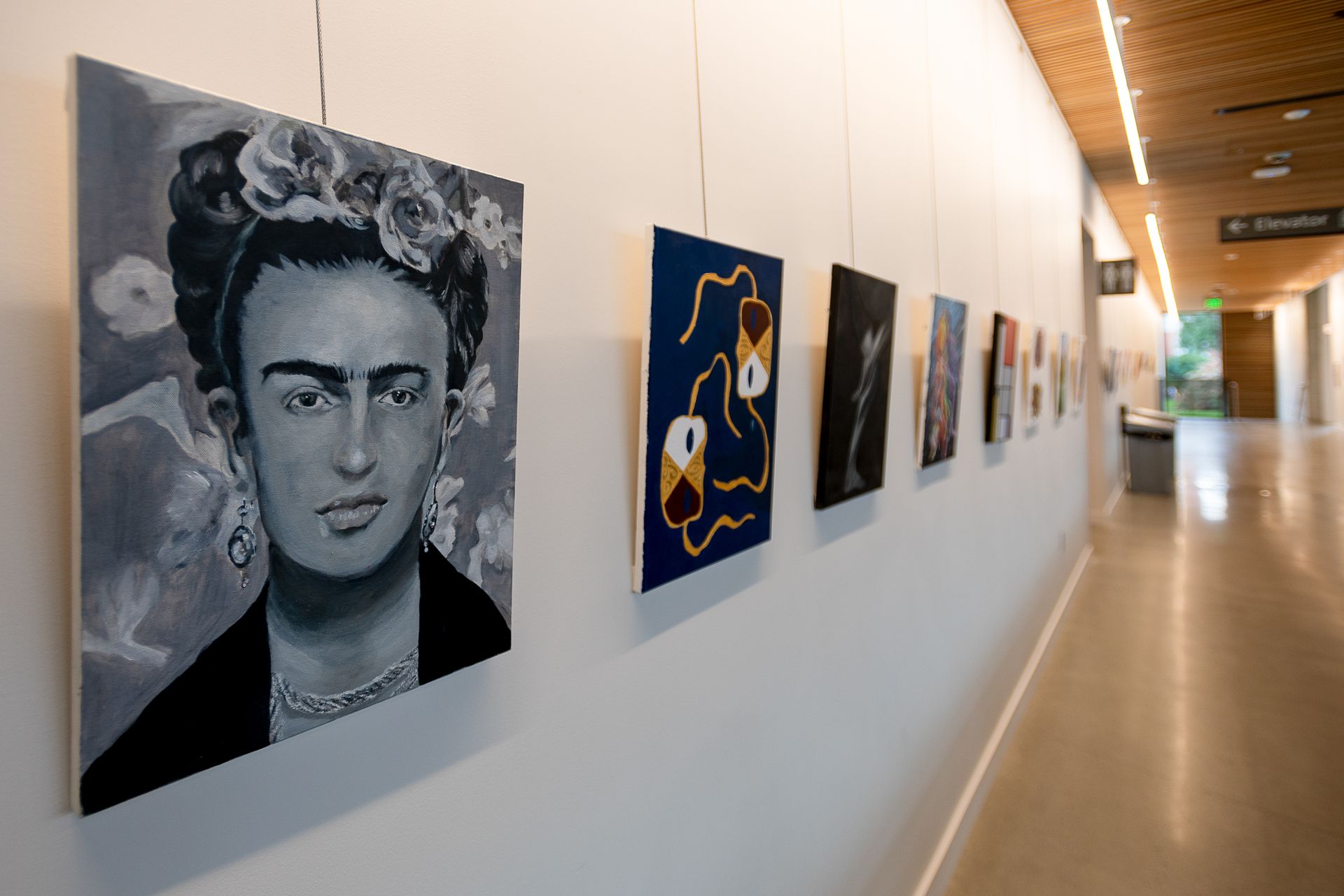 A linear perspective view of the art gallery hallway in the Shiley Marcos Center for Design and Innovation at the University of Portland, with framed paintings extending down the length of  the wall.