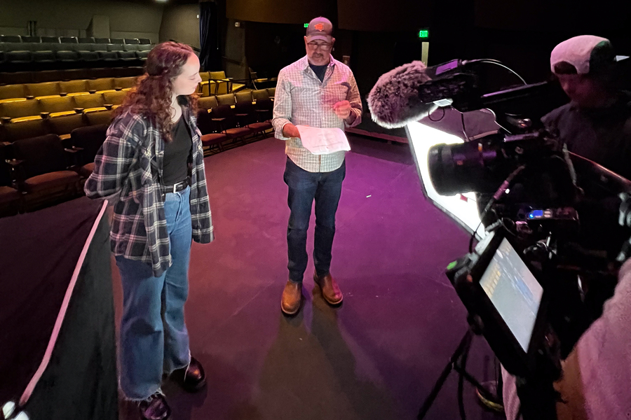 An arts administration student at University of Portland works behind the scenes of a media production in a theater.
