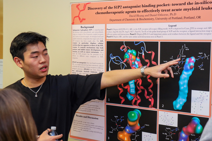 A University of Portland student stands beside his research poster as he explains the subject matter to a viewer at the Founder's Day celebration.