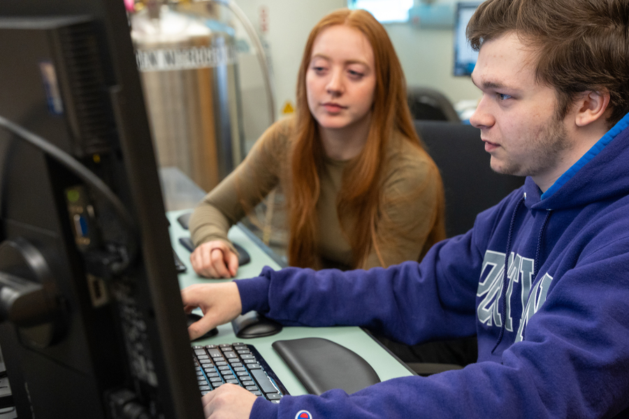A partially obscured close-up view of two UP students seated in front of a computer in the biology lab as they look intently at the screen.