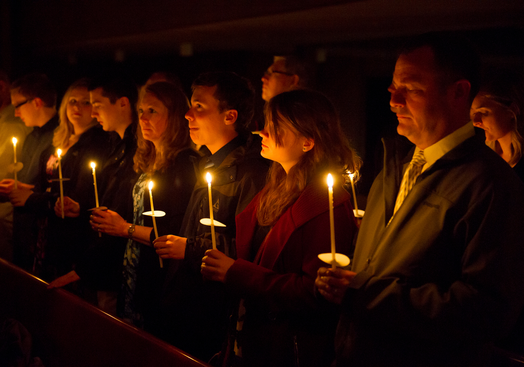 A group of University of Portland students are gathered for the nighttime Easter vigil ceremony, each holding a single candle that illuminates their faces in the darkness.