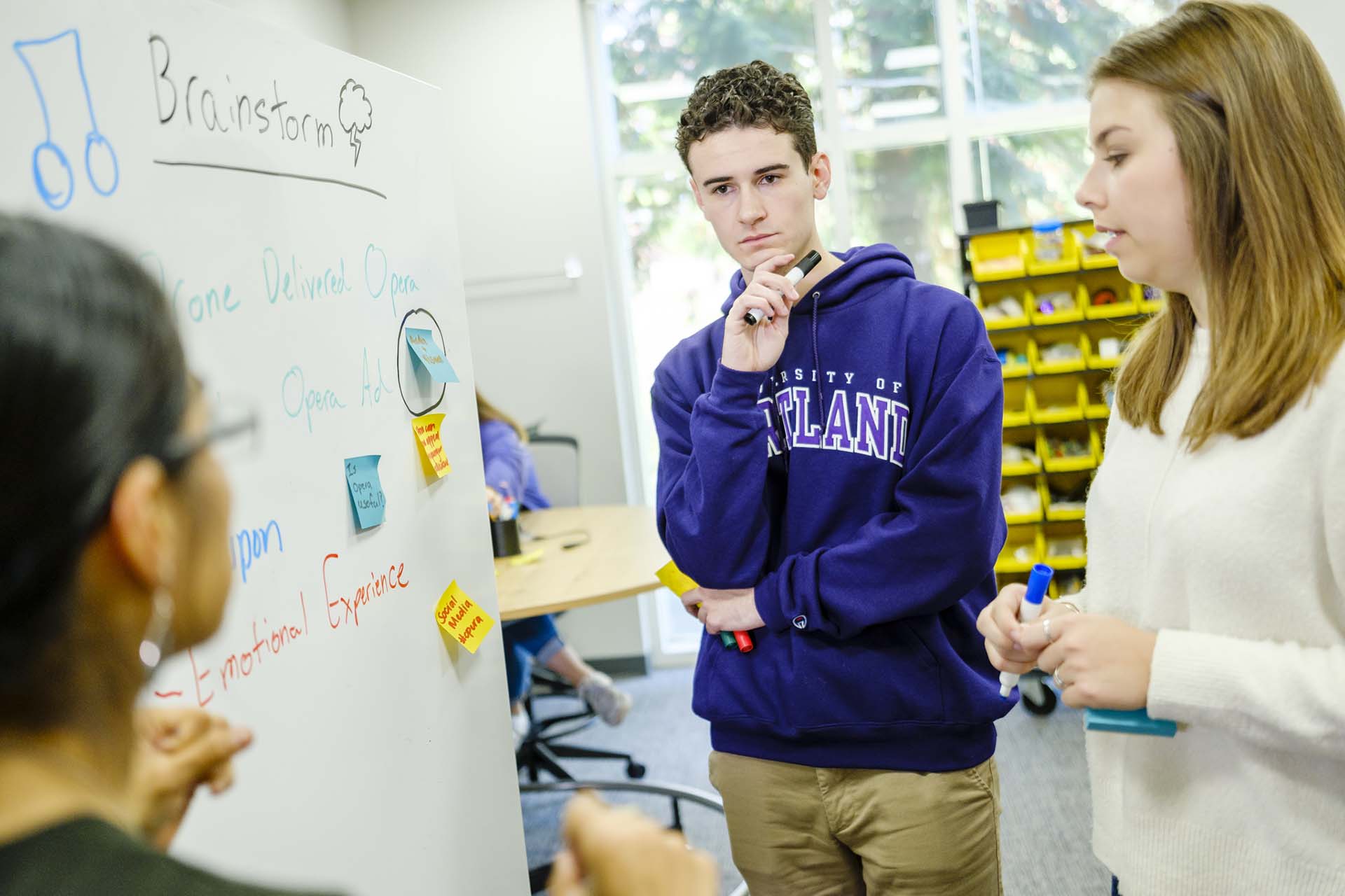 Two University of Portland business students standing before a whiteboard during a brainstorming session with their student teacher guiding them