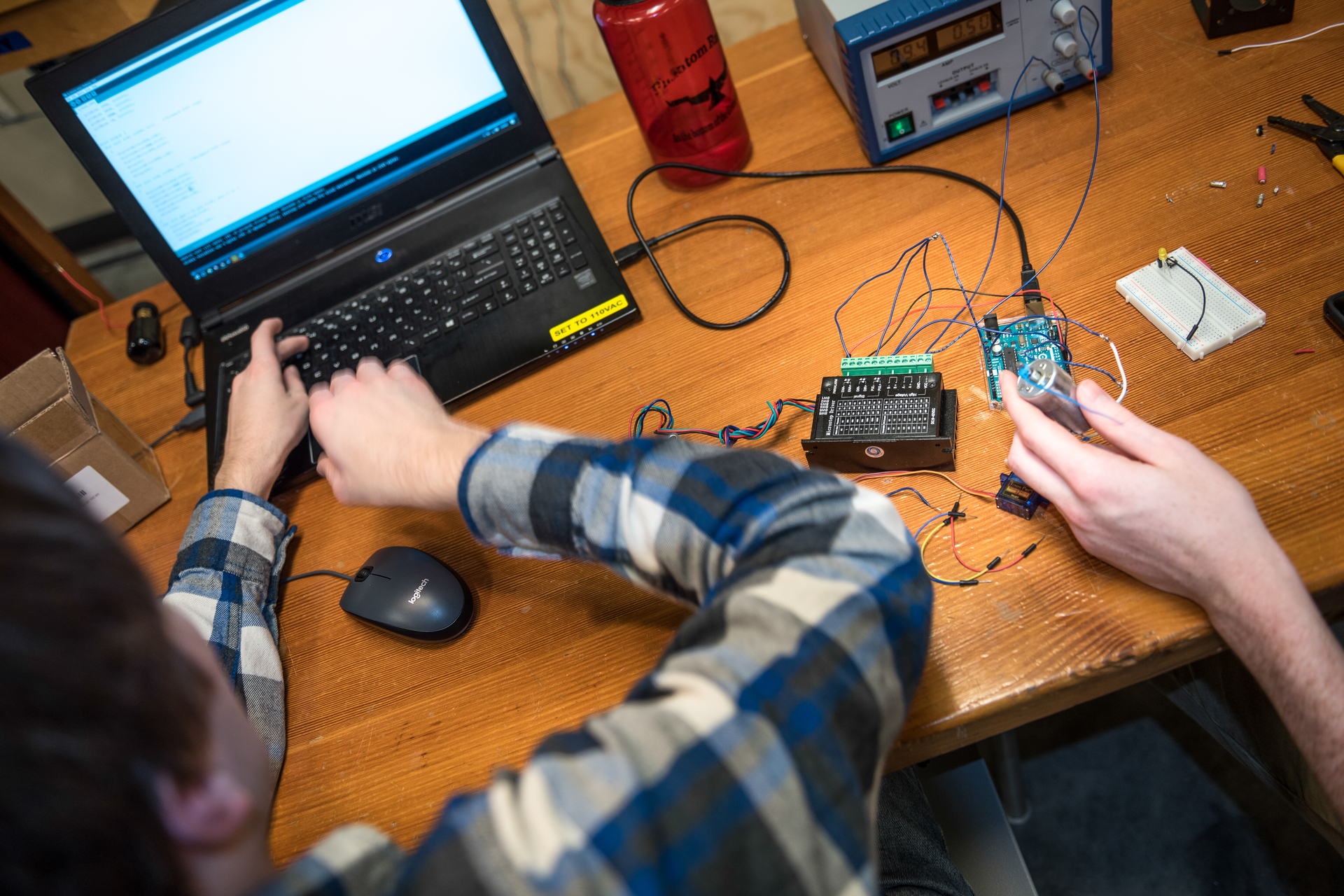 An overhead view of two students building computers in the adaptive technology class. Only their hands are visible as they manipulate circuit boards and work on a laptop at a desk in an engineering lab at University of Portland.