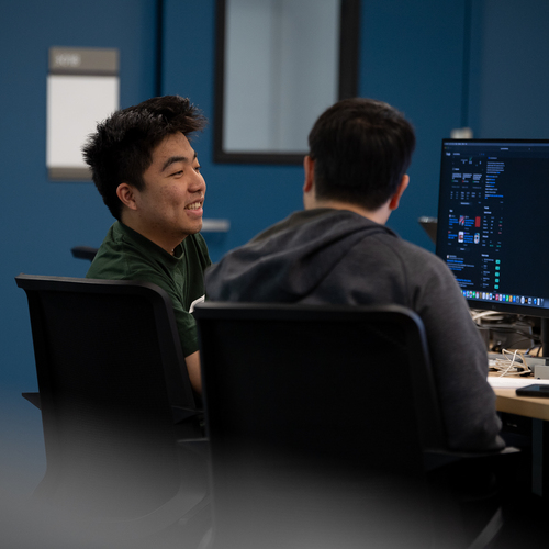 A candid image of two UP engineering students smiling as they converse while seated at a computer work station.