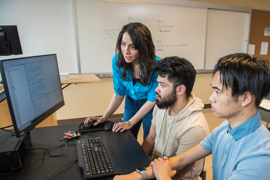 Two UP engineering students review data on a computer screen with their professor in the classroom.