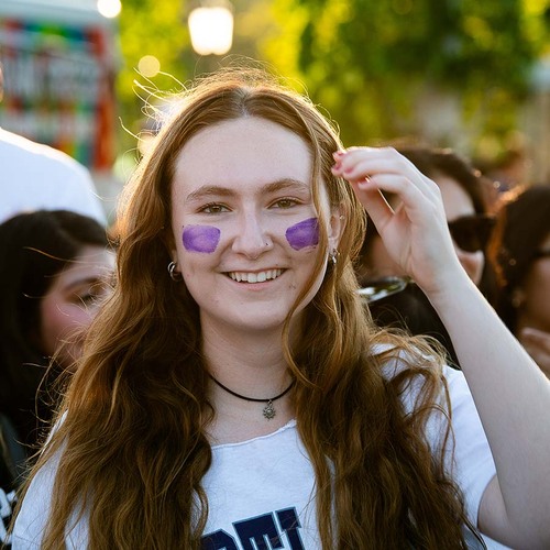 A University of Portland student gets purple stripes of face paint during the orientation soccer game.