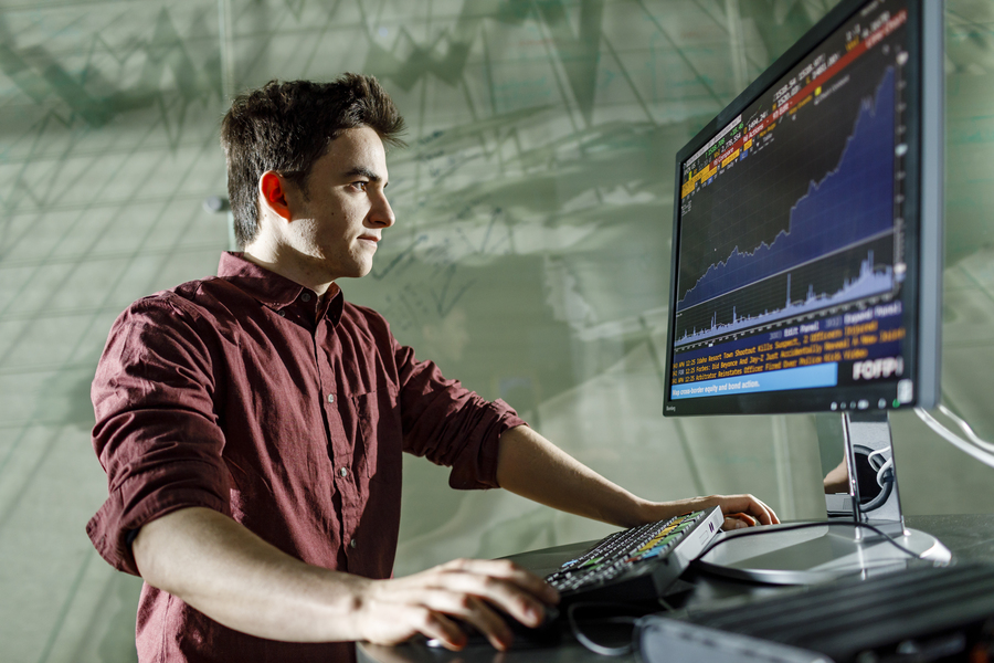 A dynamic low angle image of a student working at the Bloomberg terminal computer in the business school at the University of Portland.