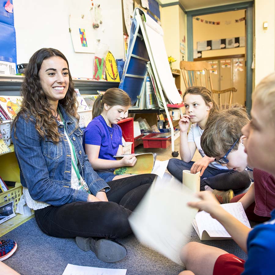 A University of Portland education student teacher sits on the floor with her elementary class and listens with a smile as one of the students asks her a question