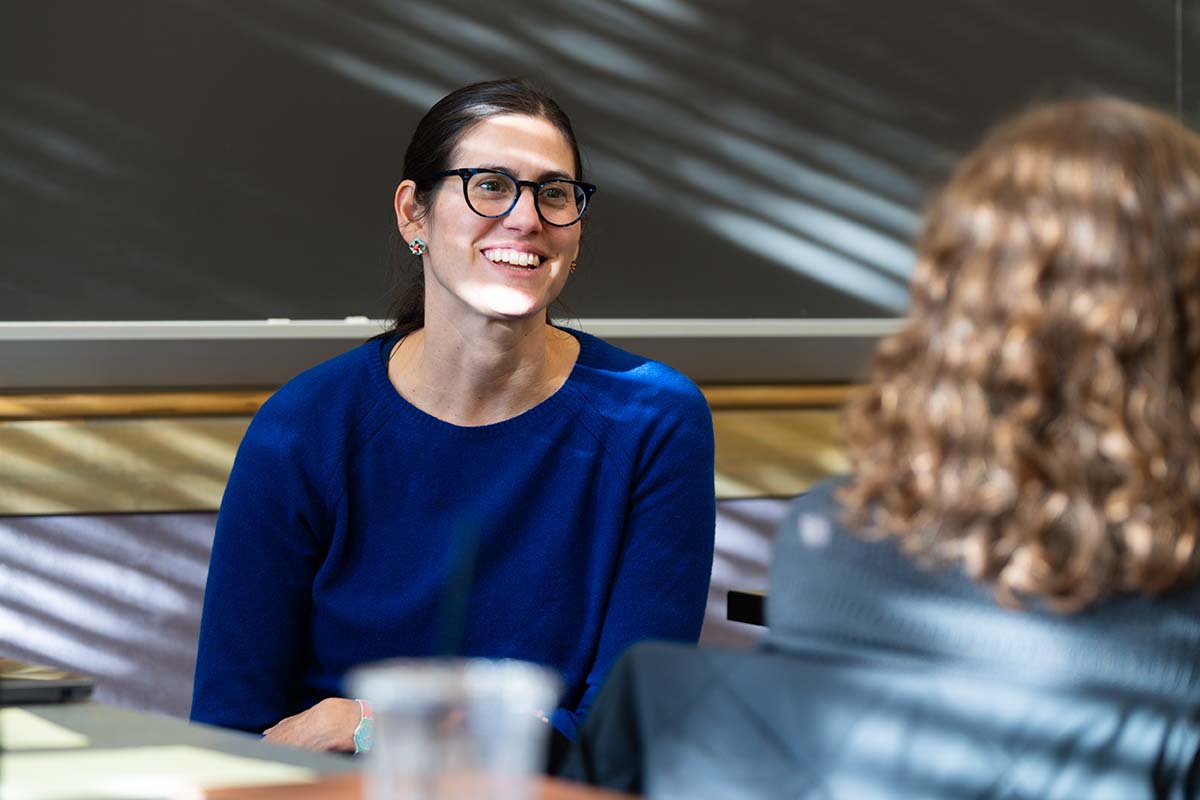A University of Portland Professor of Education smiles at students as she sits in front of the blackboard in class