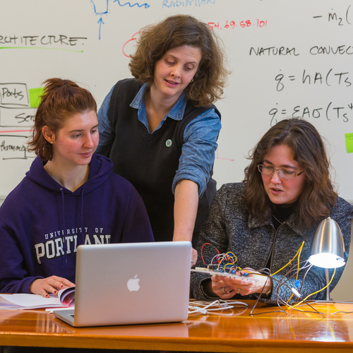 A UP engineering professor stands behind two students seated in a classroom, pointing at the screen of their computer providing guidance as they work.