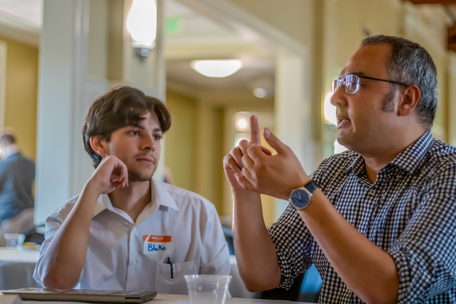 A UP engineering student with brown hair, wearing a white collared shirt, sits at a table with a professor listening pensively while they converse.
