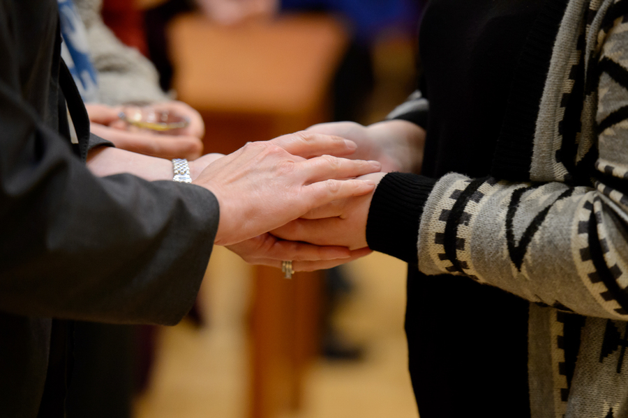 A close up image of the hands of a priest holding the outstretched hands of a congregant during a blessing of hands ceremony at the Chapel of Christ the teacher at the University of Portland.