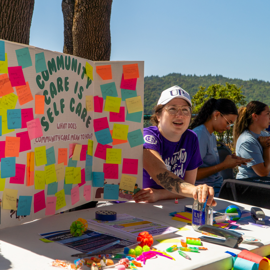 A display board with large green letters partially reading “COMMUNITY IS CARE” and colorful sticky notes with handwritten messages attached to the right side.