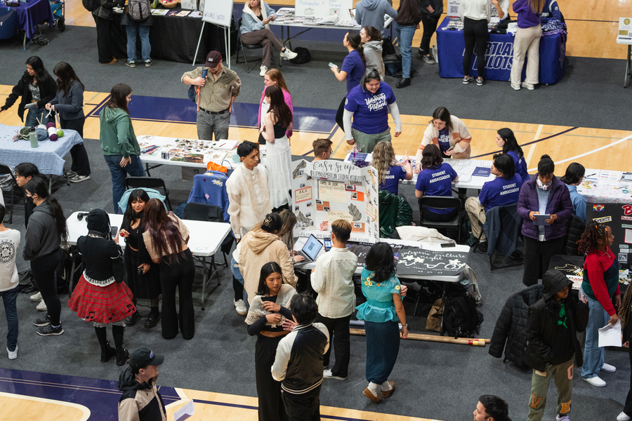 A group of UP students sit at a table with laptops in front of a display board for the Filipino American Student Association at student activity fair. The board is decorated with text, images, and illustrations.