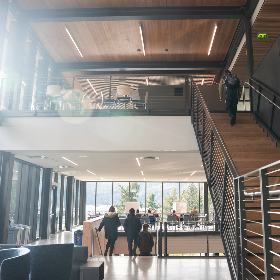 A section of the Shiley Marcos Center for Design and Innovation with a modern ceiling with recessed lighting and an air vent, with large windows and trees visible outside in the background.
