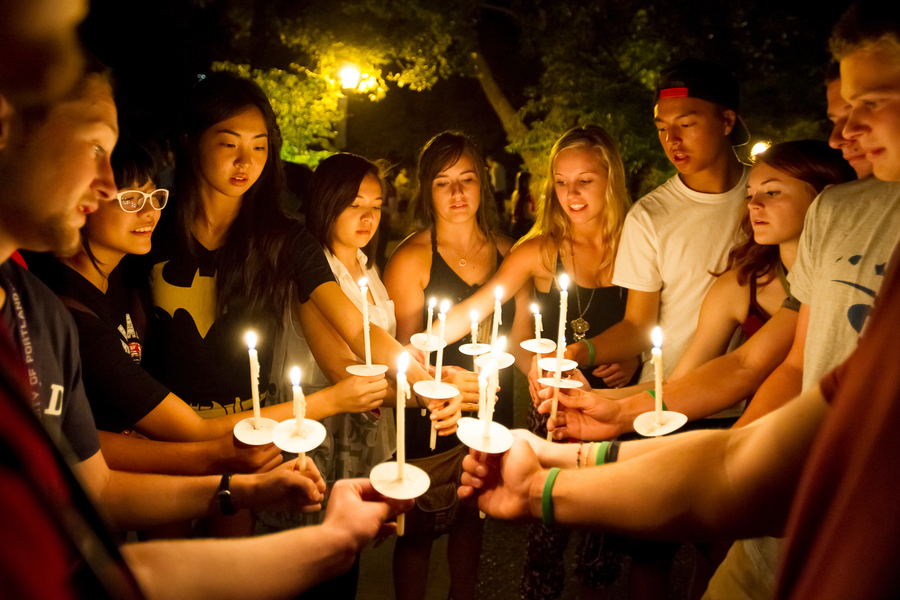 A group of University of Portland students are gathered in a close circle, each holding a lit candle, at the bell tower ceremony.