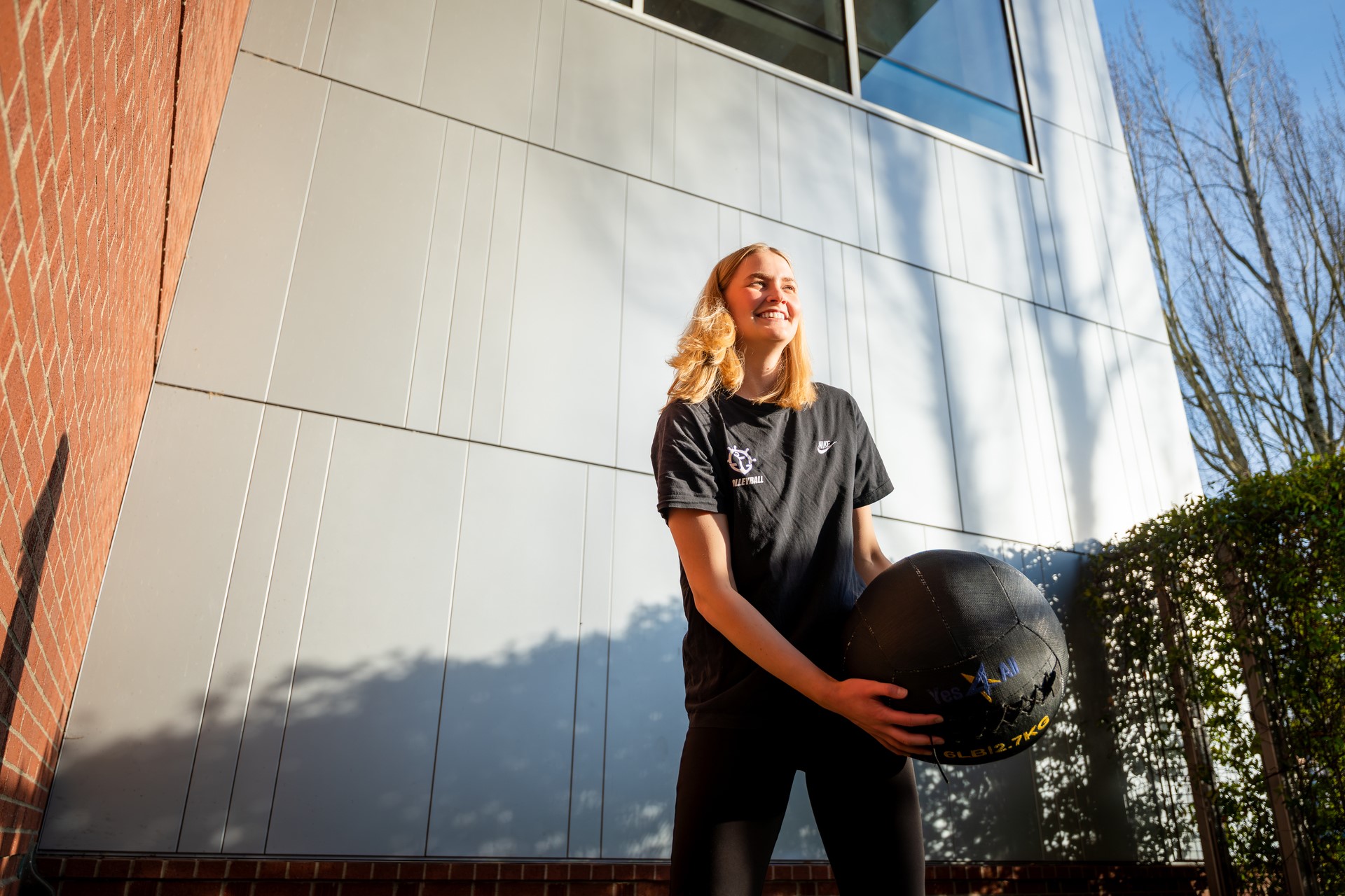 A student tosses a medicine ball in the sunlit outdoor exercise area at UP's Beauchamp recreation center.