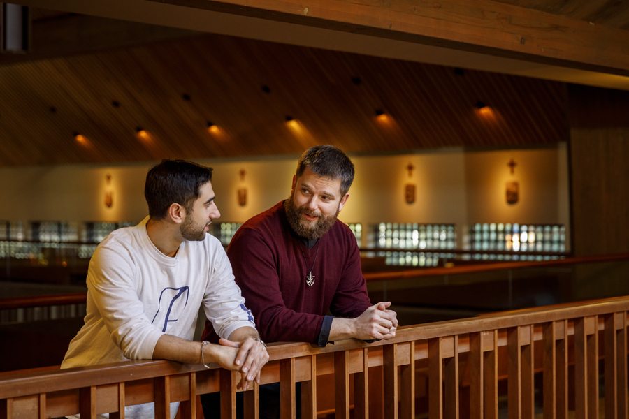 A student and priest converse casually in the Chapel of Christ the Teacher at the University of Portland.
