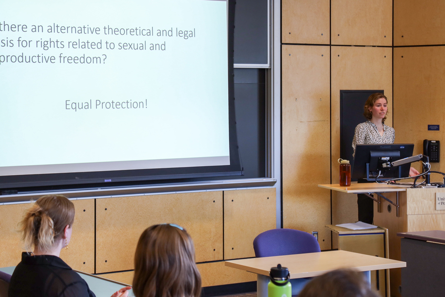 A UP student is standing at a podium giving a presnetation. Ther is partial text on the screen to her left that describes equal rights and protections.