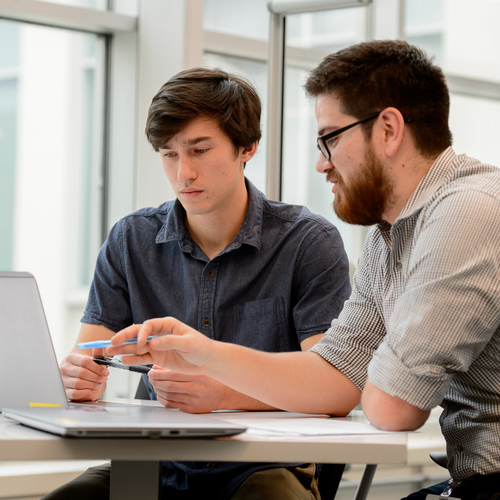 A UP student with their mentor are seated at a table looking intently at a computer screen. The image is focused on the upper half of their bodies.