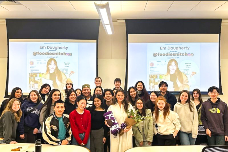 UP entrepreneurship students gather in front of a classroom projector screen displaying a fellow student's social media page during a university event.