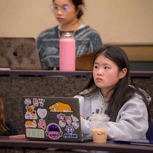 A UP business student sits behind a desk with an open laptop computer while listening intently during a finance class.