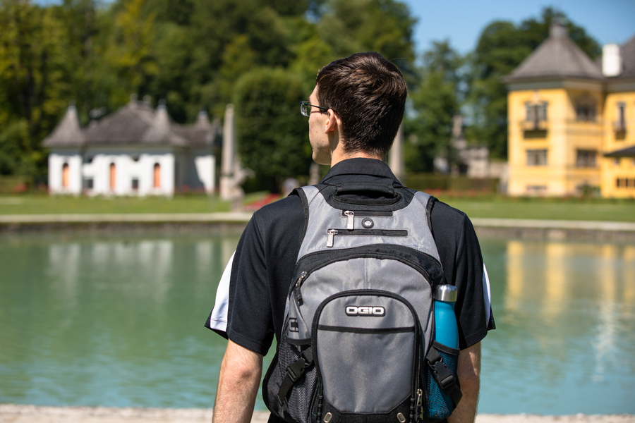 A University of Portland student stands in foreground, facing away from the camera, looking at a scenic lake surrounded by historic buildings in Austria during a study abroad experience.