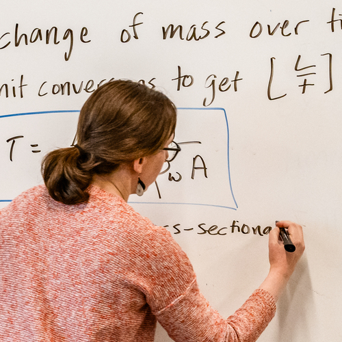 A University of Portland engineering professor, seen from behind, write notes on a whiteboard during an environmental engineering class.