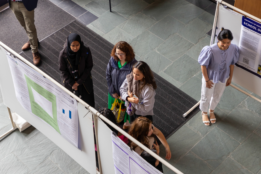 An aerial image of students in an exhibit hall gathered around a research poster at the undergraduate research fair at the University of Portland.